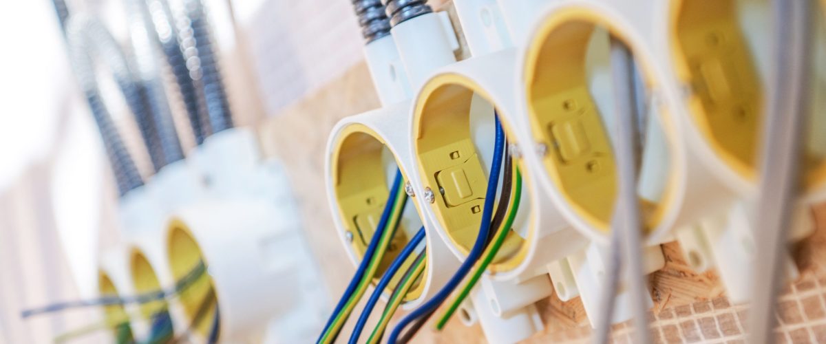 Multiple electrical outlets are attached to a wooden wall, showcasing various colored wires extending from each outlet, ready for installation.